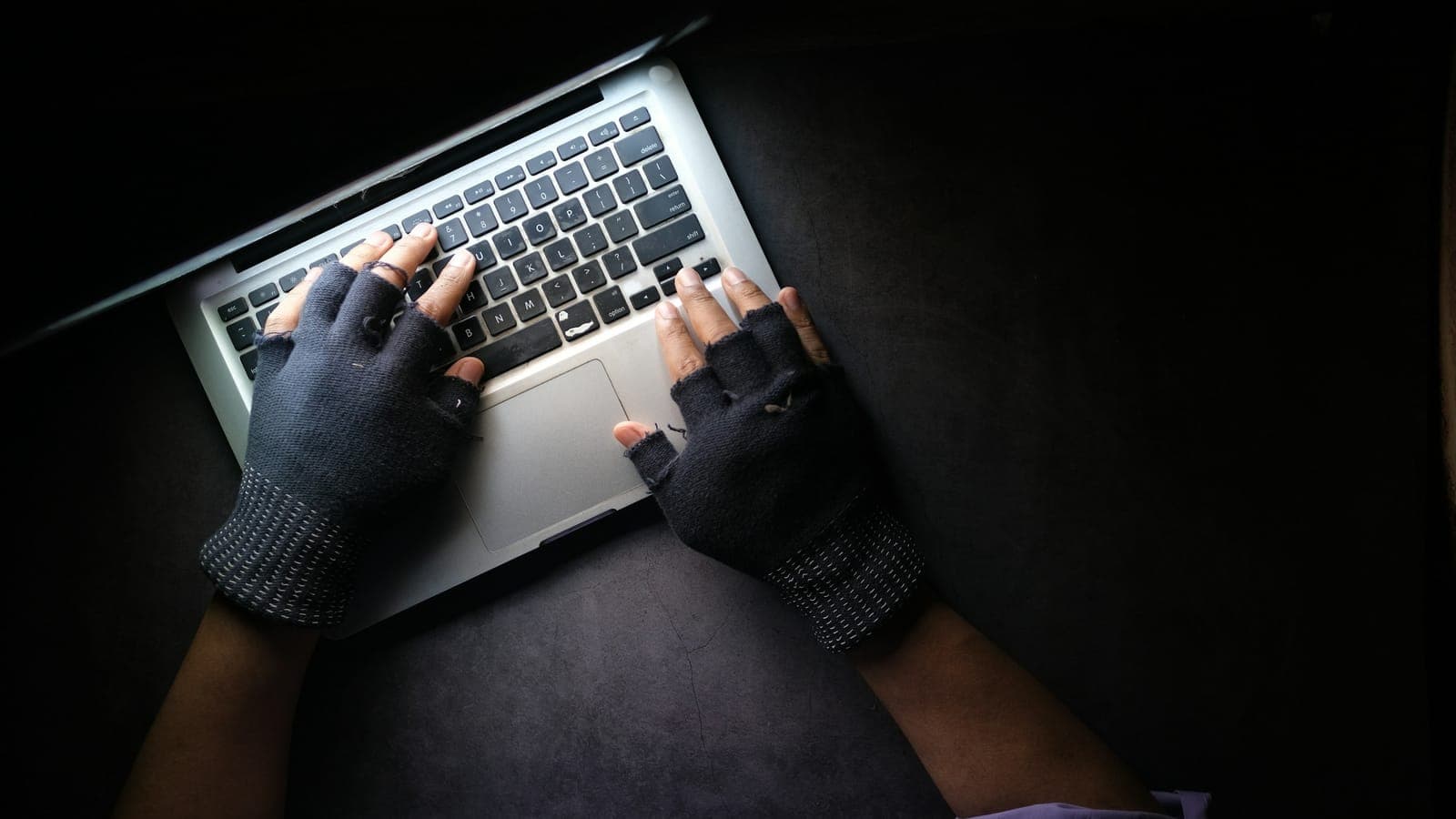 Mains gantées tapant sur le clavier d'un ordinateur portable dans la pénombre