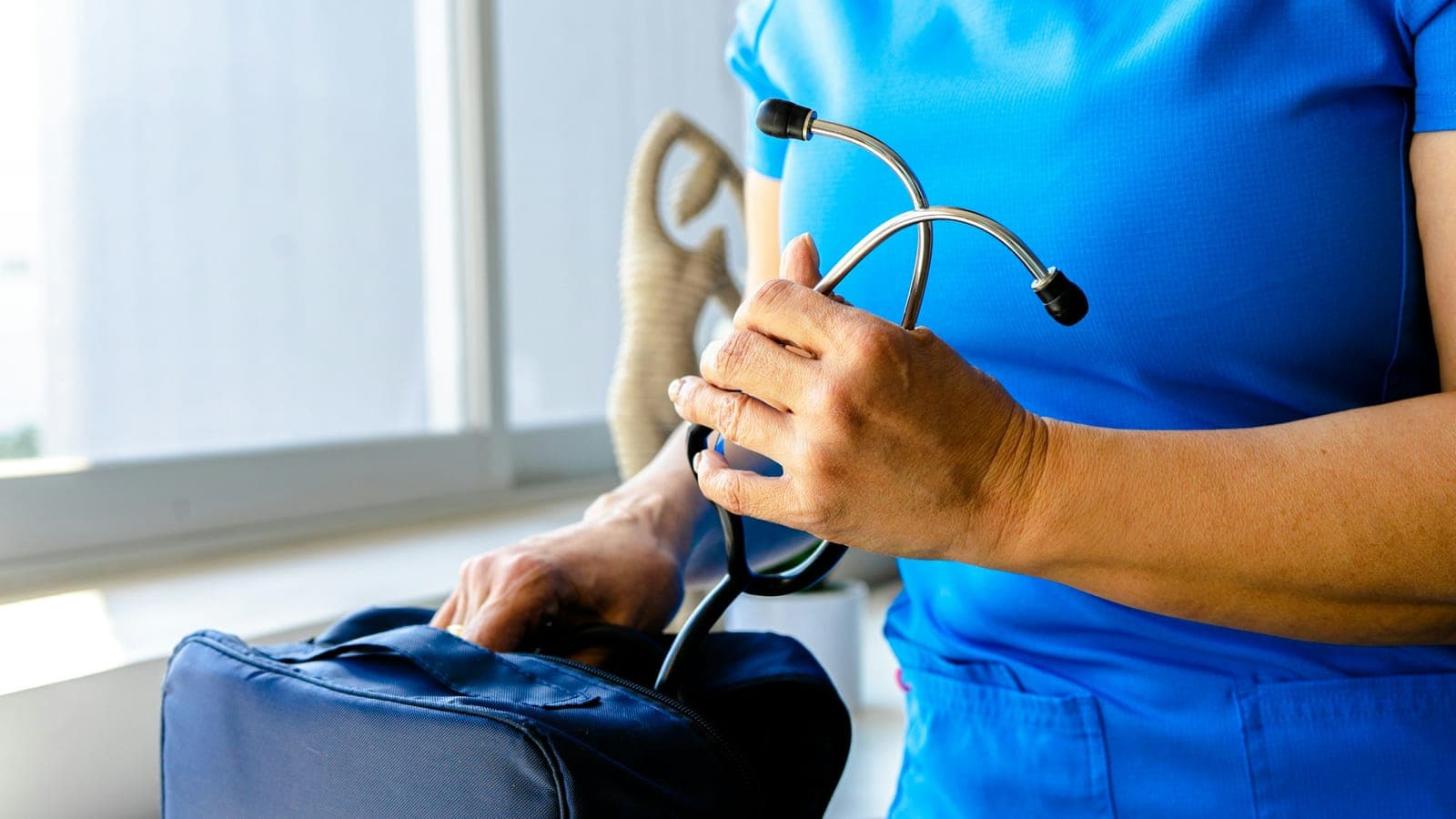 Infirmière en tenue bleue tenant un stéthoscope au-dessus de sa sacoche de soins