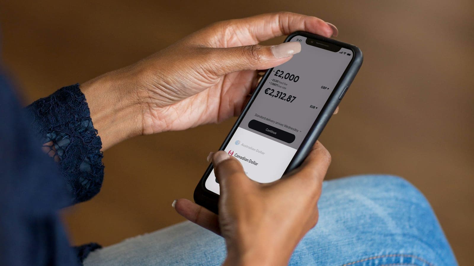 Mains tenant un téléphone affichant une application de transfert d'argent avec une conversion de devises
