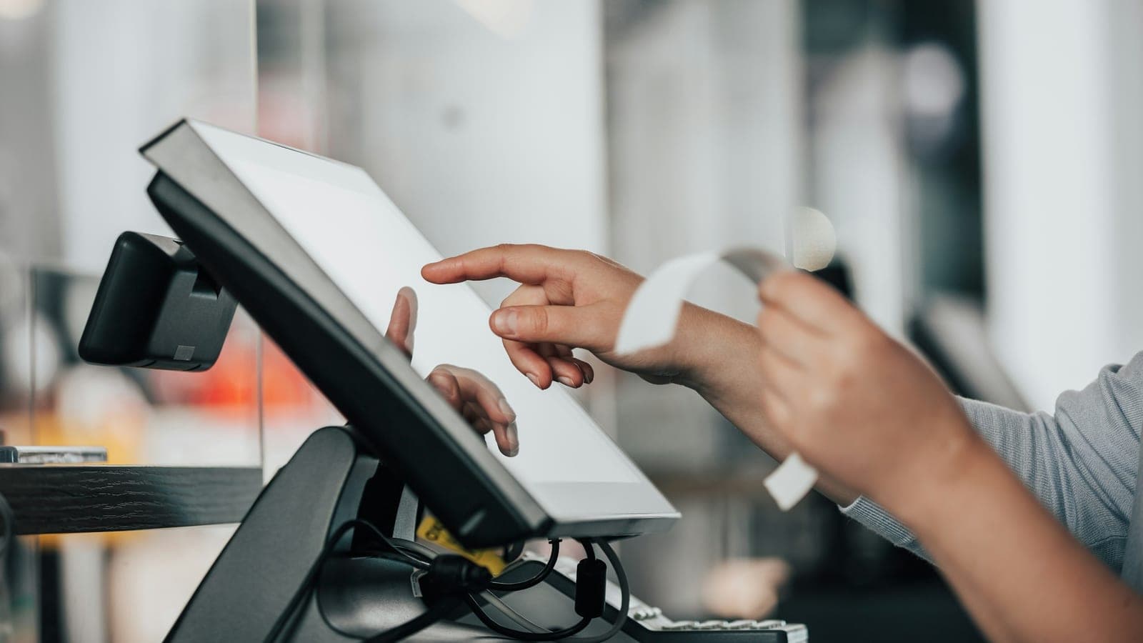 Mains utilisant une caisse tactile et détachant un ticket de caisse dans un commerce