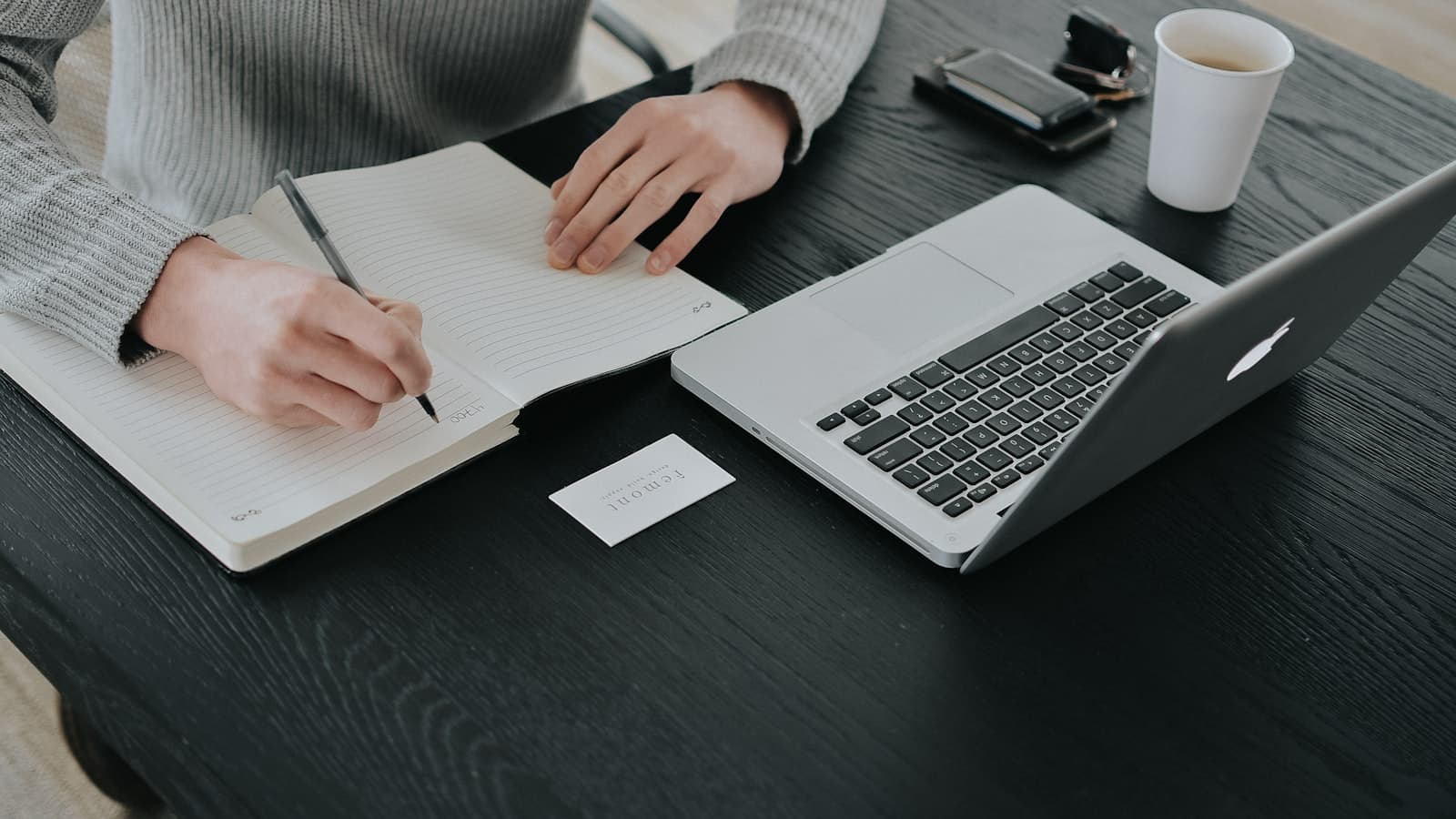 Indépendant prenant des notes dans un carnet devant son ordinateur portable