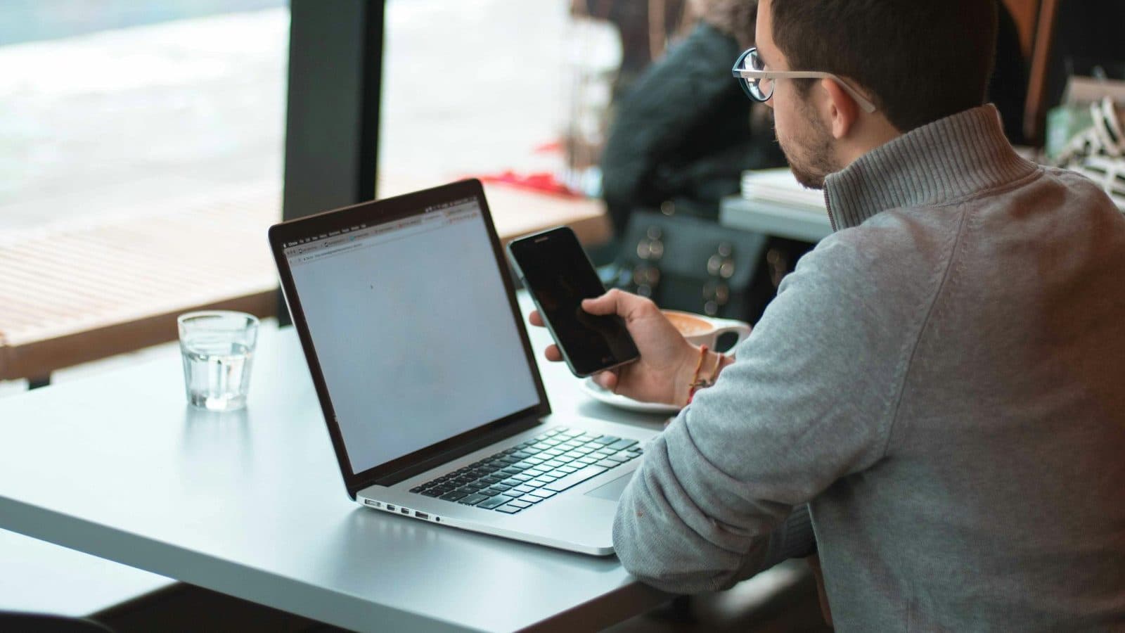 Freelance travaillant sur son ordinateur portable et son téléphone à la table d'un café, près de la vitrine