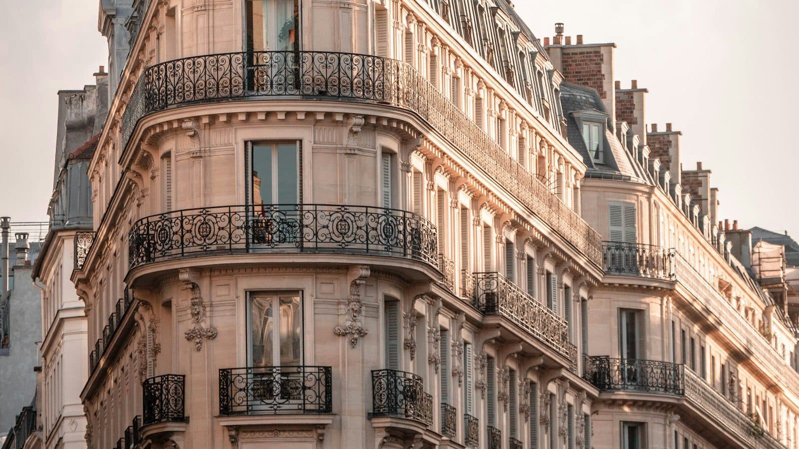 Immeuble haussmannien d'angle avec balcons en fer forgé, dans la lumière du soir