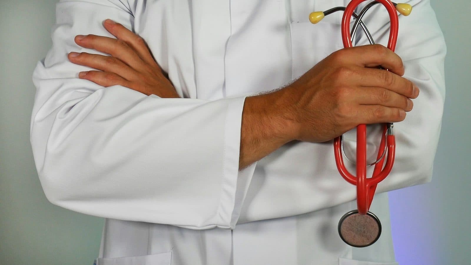 Médecin en blouse blanche, bras croisés, un stéthoscope rouge à la main