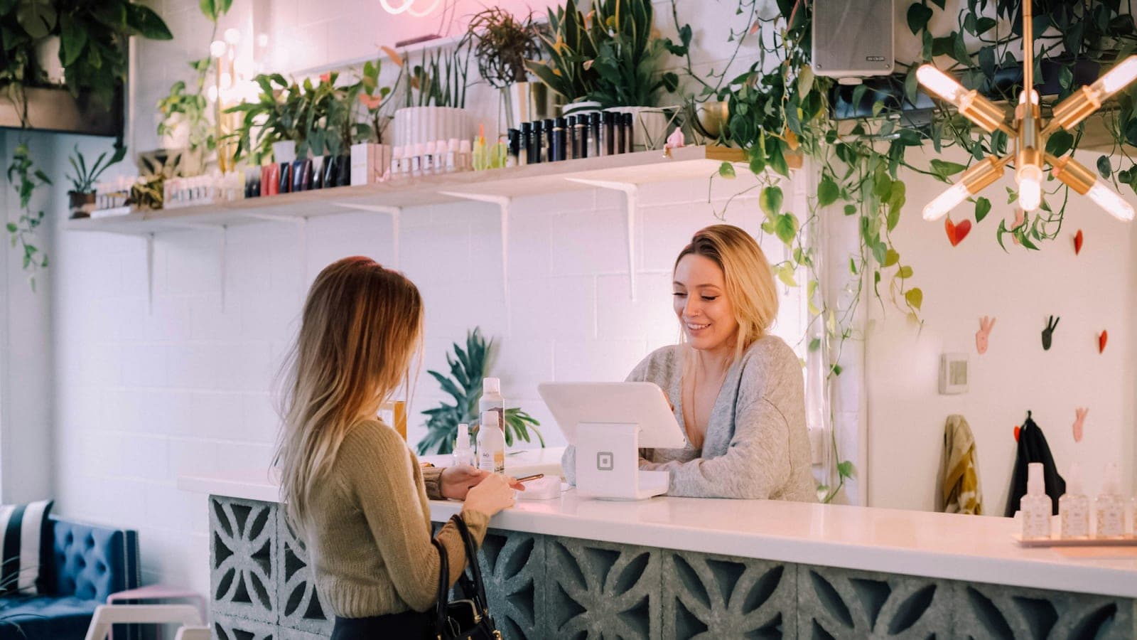 Commerçante encaissant une cliente au comptoir de sa boutique, devant un terminal de paiement sur tablette