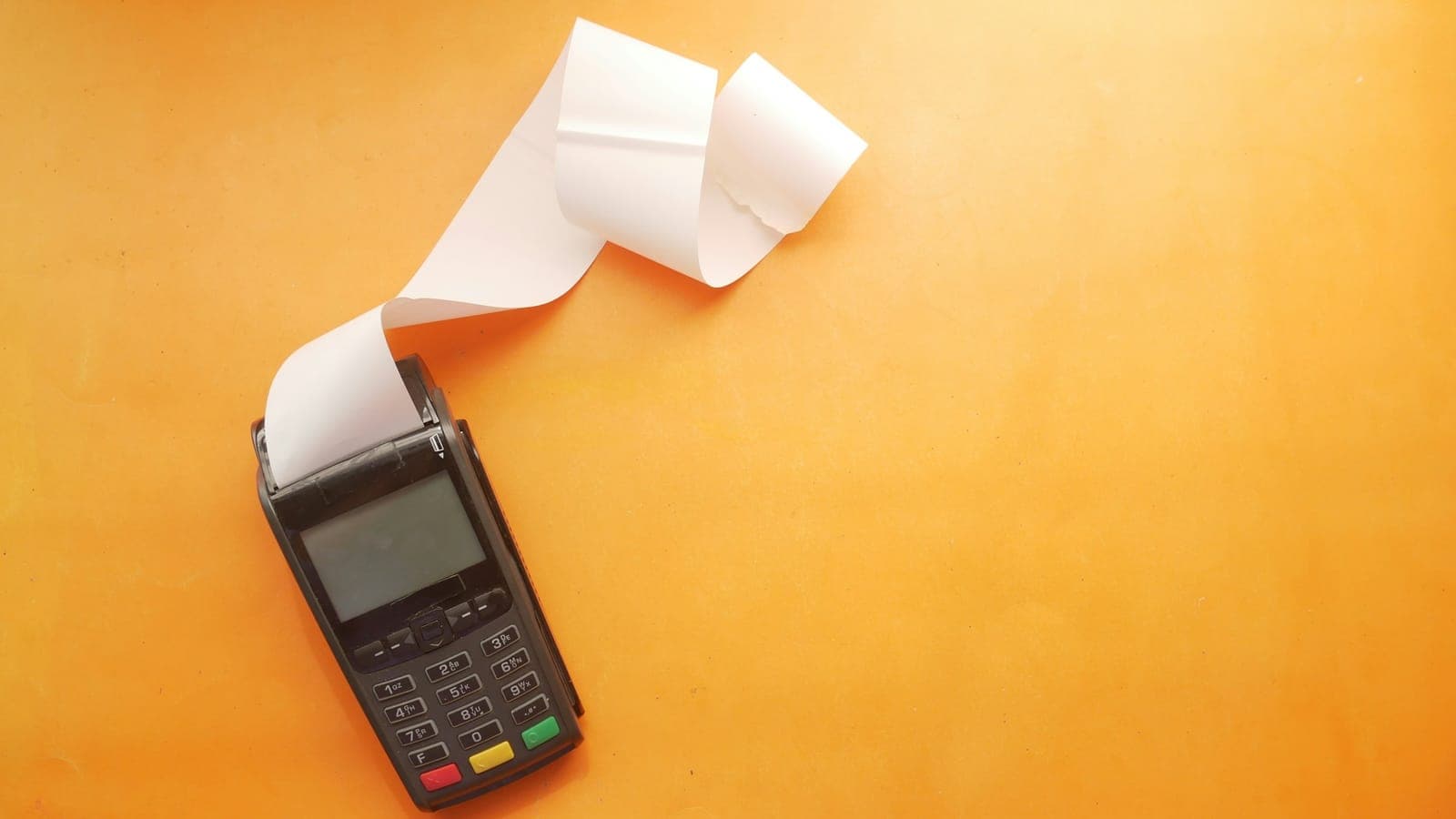 Terminal de paiement par carte imprimant un long ticket sur fond orange