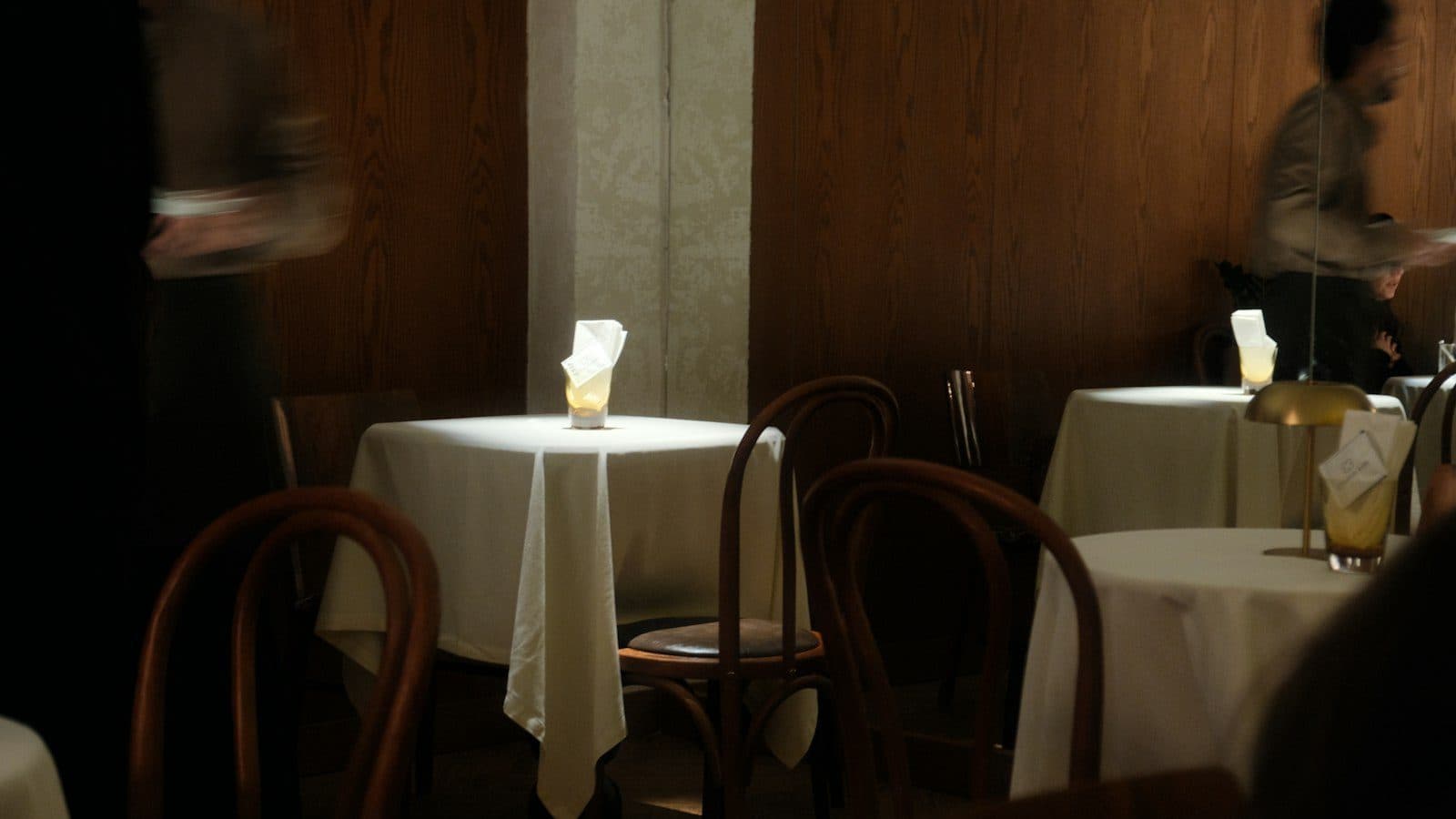 Salle de restaurant feutrée, tables nappées de blanc et chaises bistrot en bois