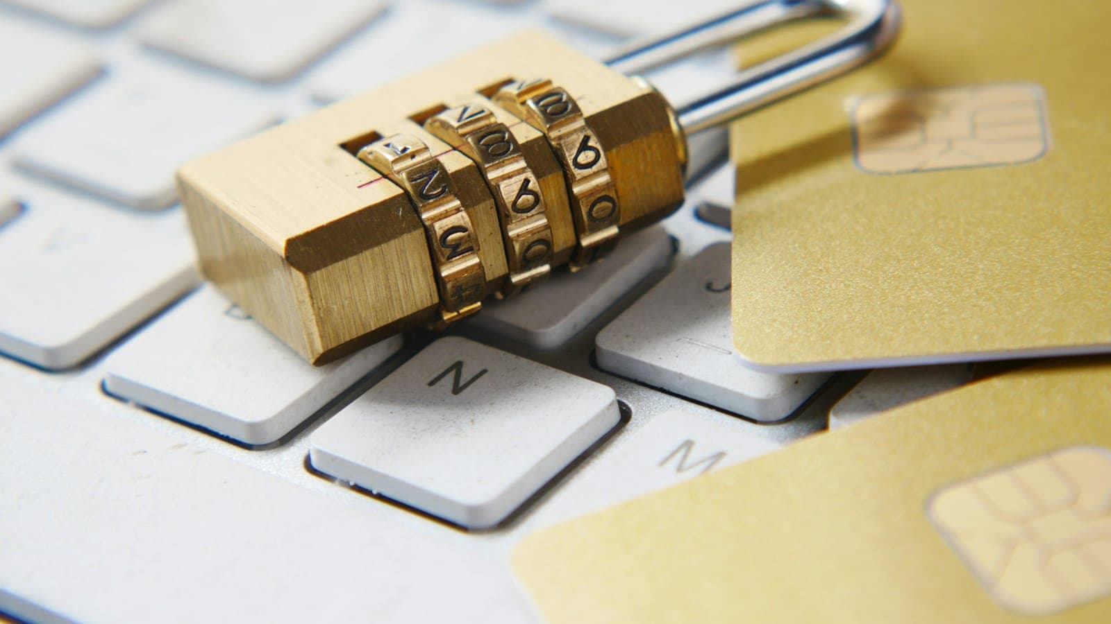 Cadenas à combinaison doré posé sur un clavier d'ordinateur clair, à côté de cartes à puce dorées