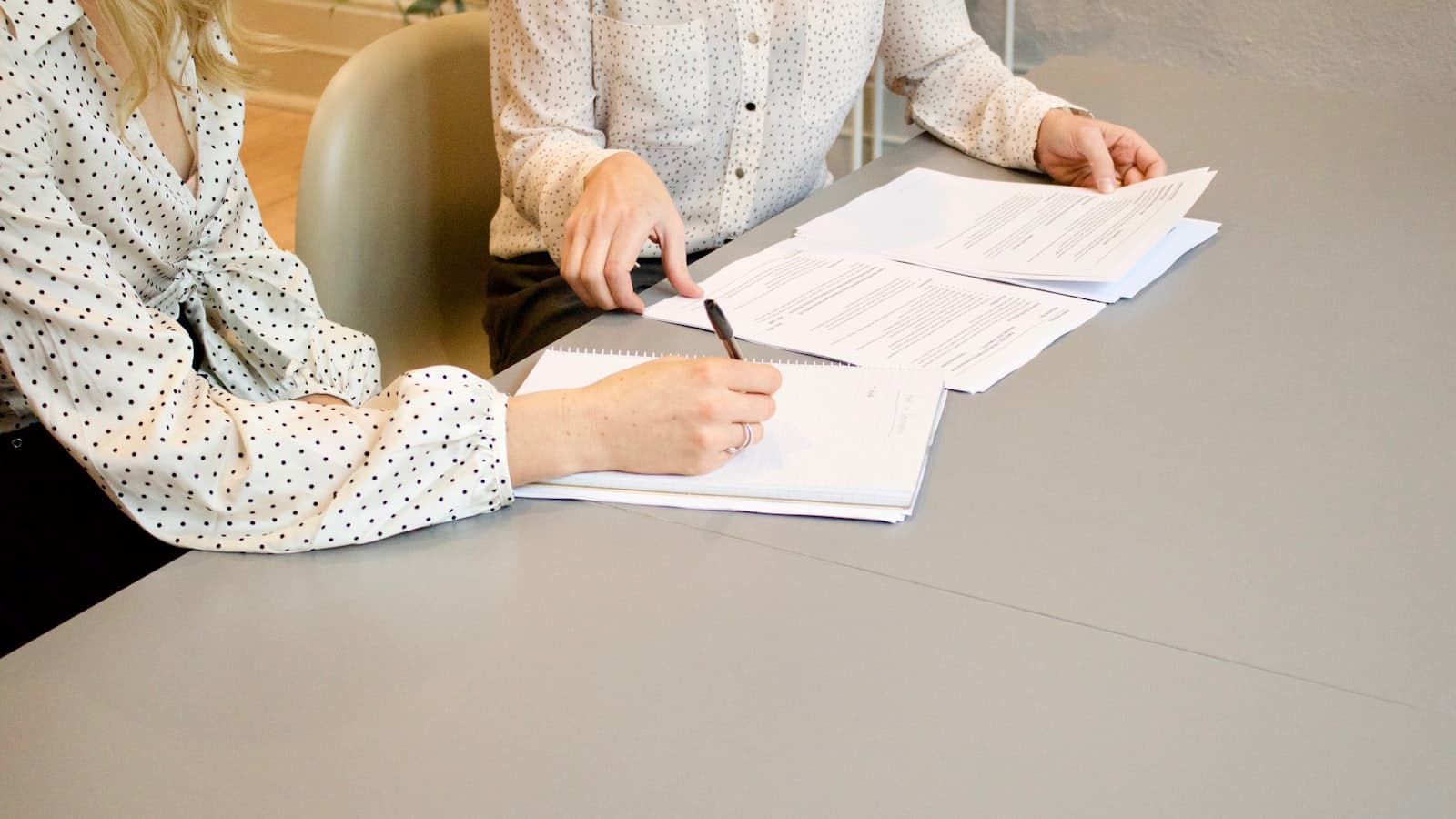 Deux personnes signant des documents de part et d'autre d'une table de réunion