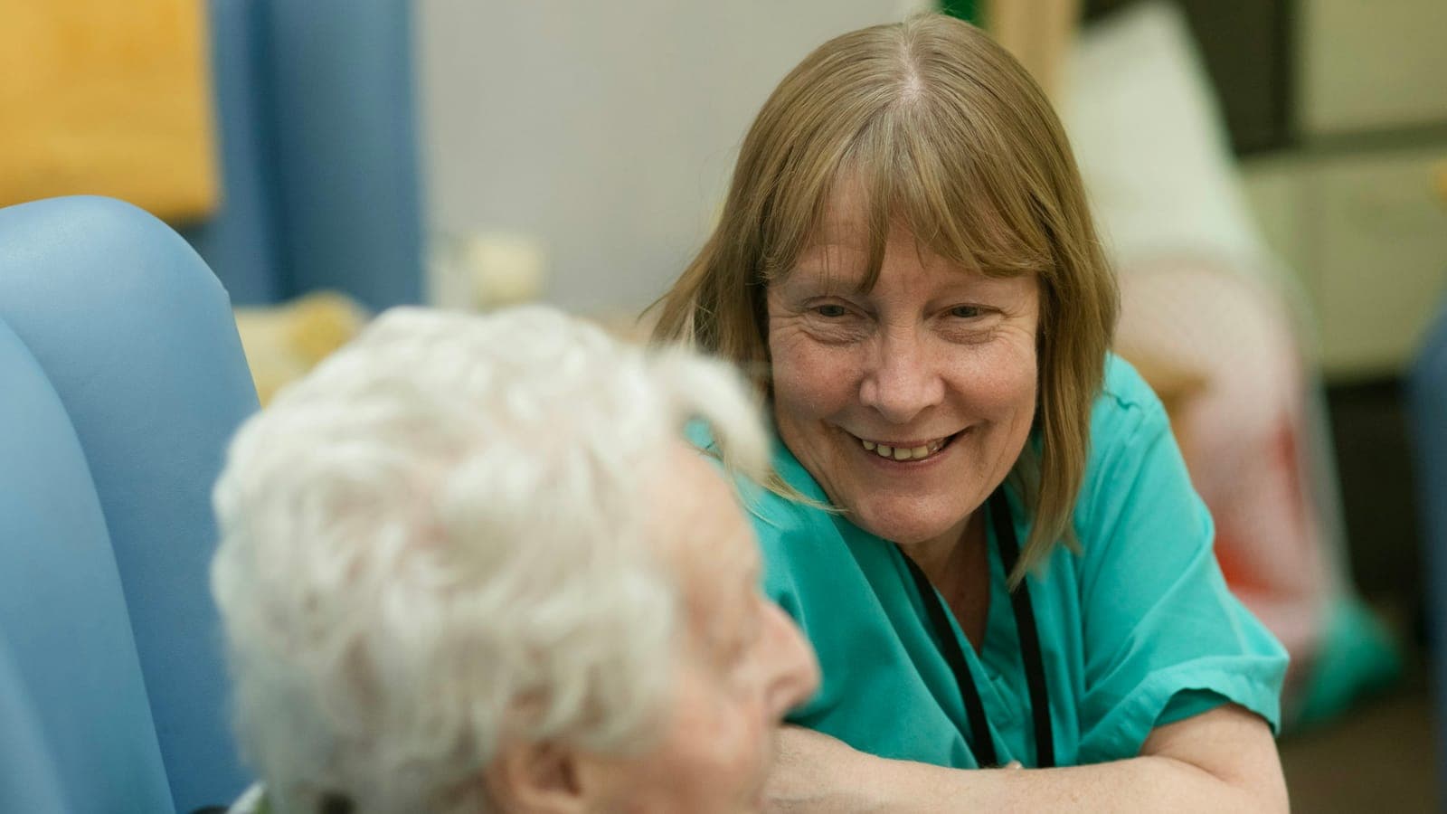 Infirmière en blouse verte souriant à une patiente âgée assise