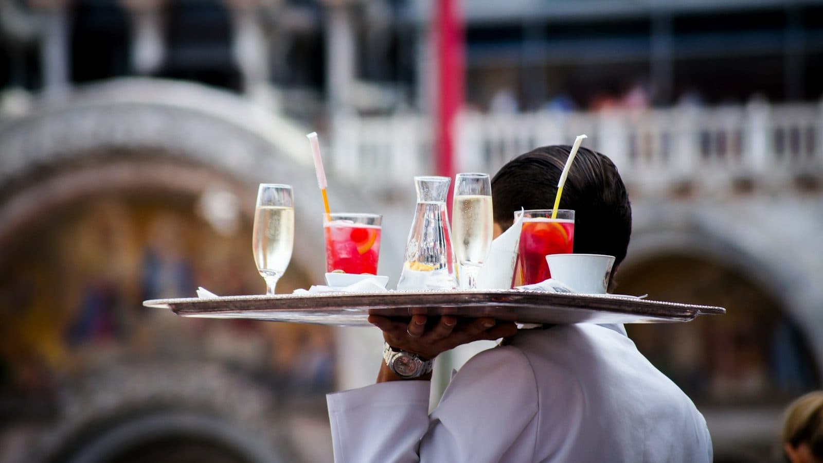 Serveur de dos portant un plateau de boissons en terrasse