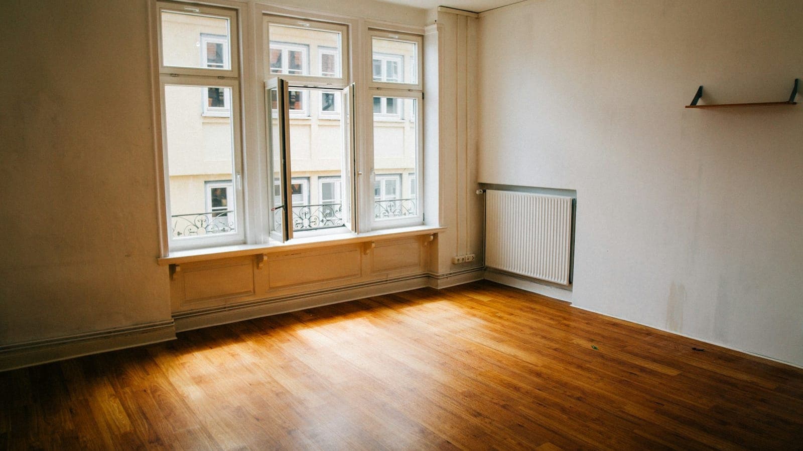 Pièce vide d'un appartement ancien, parquet en bois, grandes fenêtres et radiateur